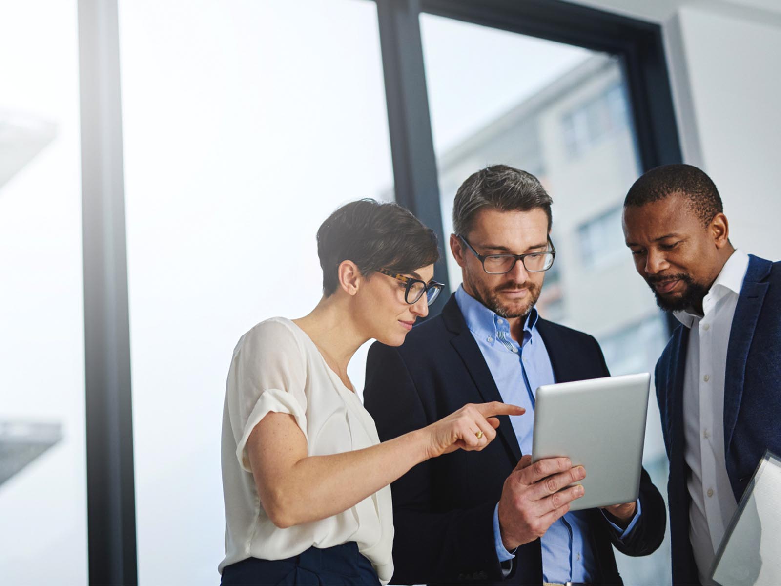 Two men and a woman in an office discussing using a hand held device 