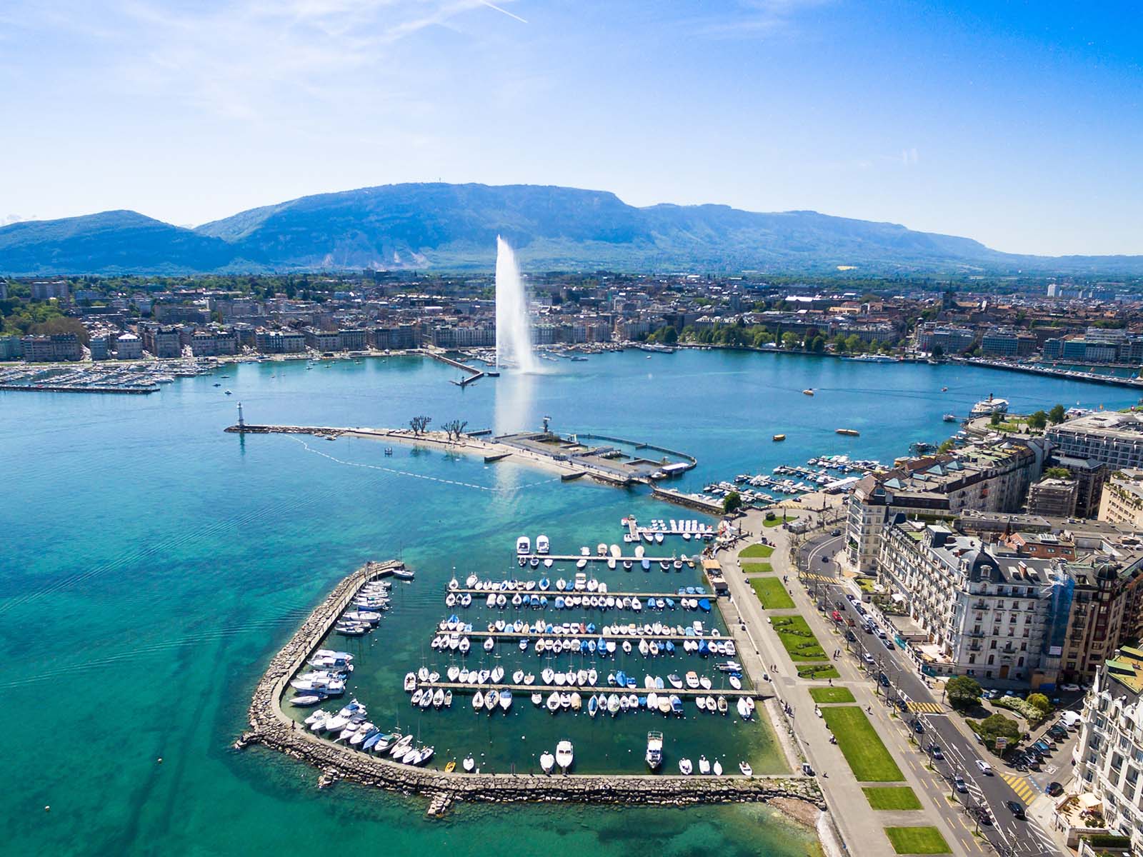 An image of  habour with a busy road next to it. There is a fountain in the distance