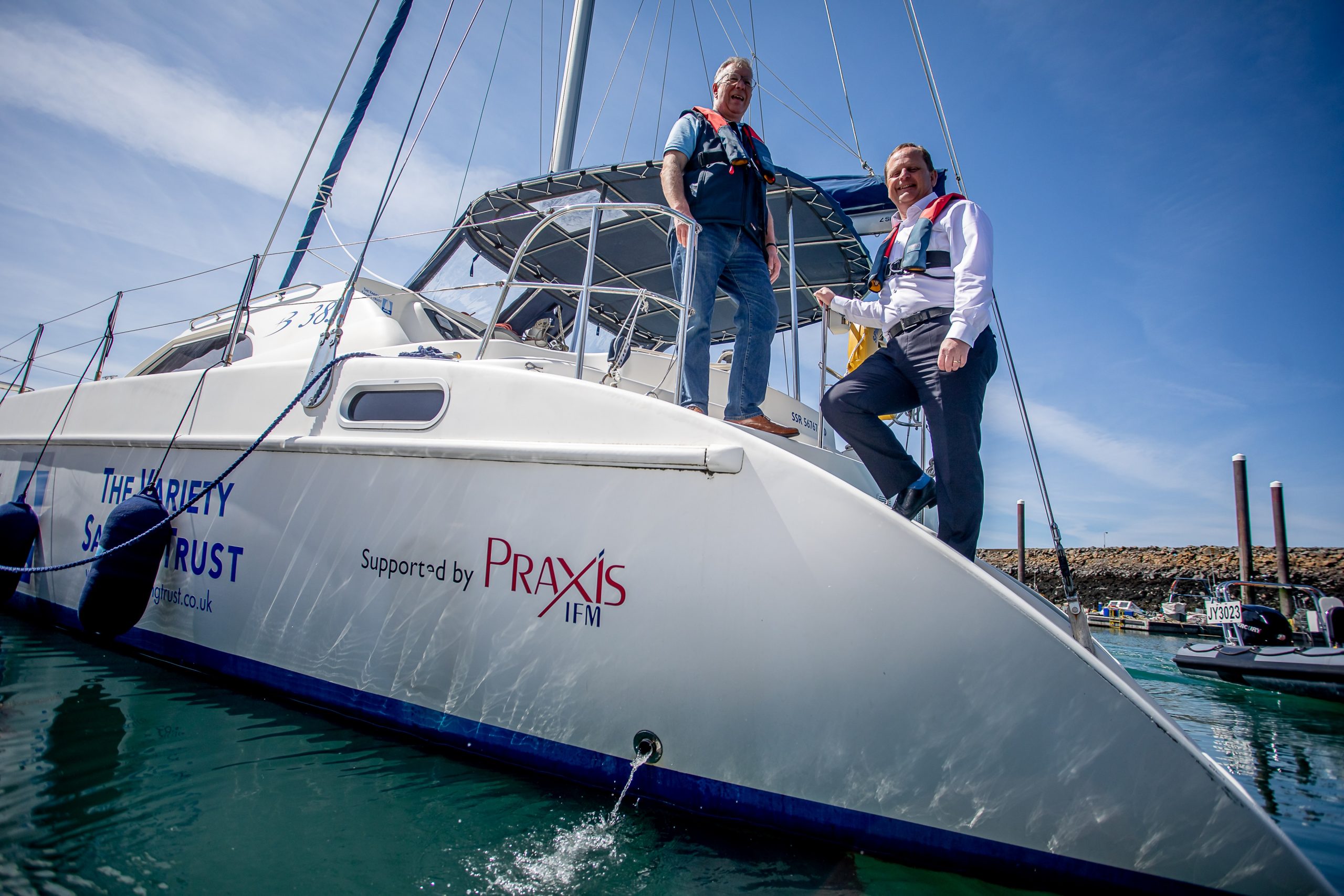 Two men stood on a sailing boat with life jackets on.