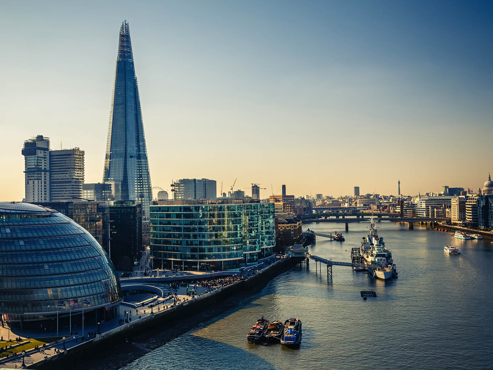 The River Thames with boats floating in it. Many modern London offices to the side of the river