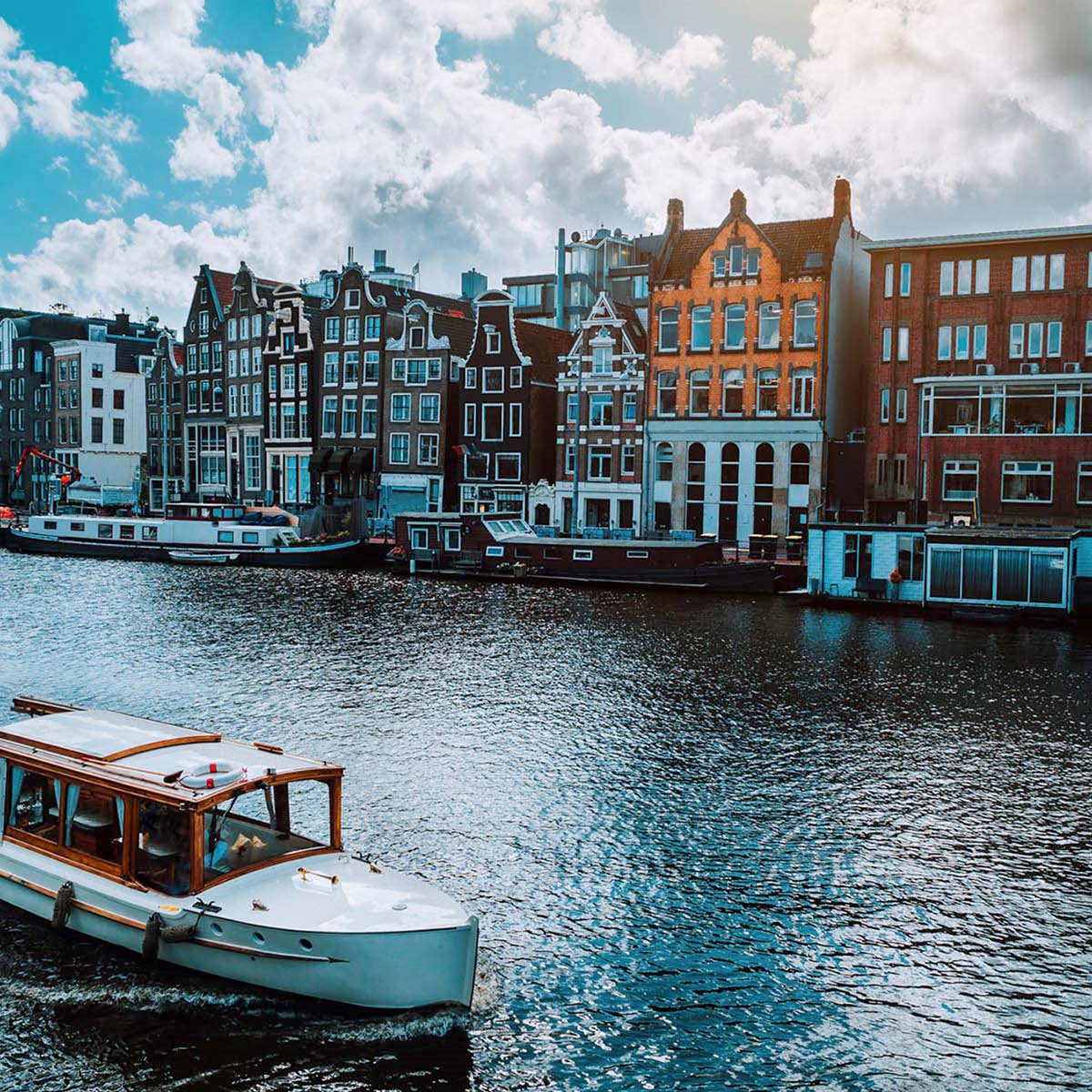 A river with many house boats floating through. Colourful buildings in the background.