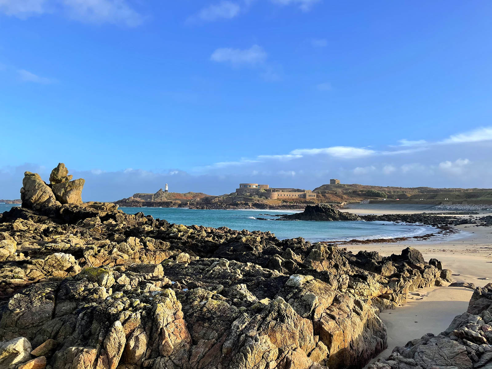 An image of a beach with many rocks. A castle is also visible in the distance